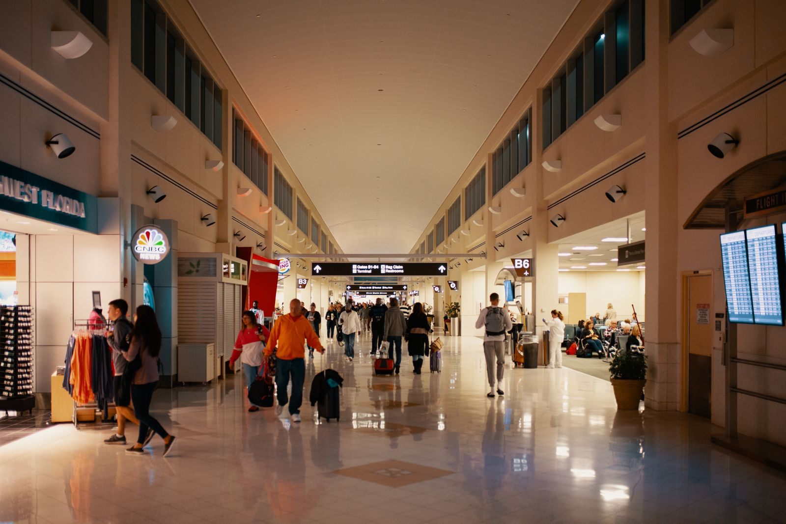 Passengers who arrive at the airport early walking with bags down a long, sunlit concourse
