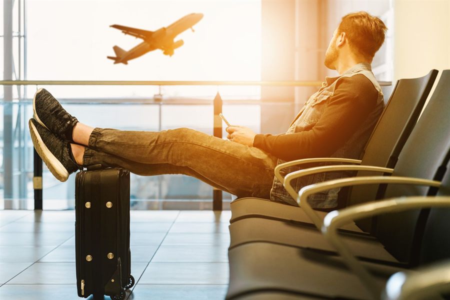 Traveler resting his feet on a carry-on at the gate while a plane takes off outside, after booking a flight at the right time