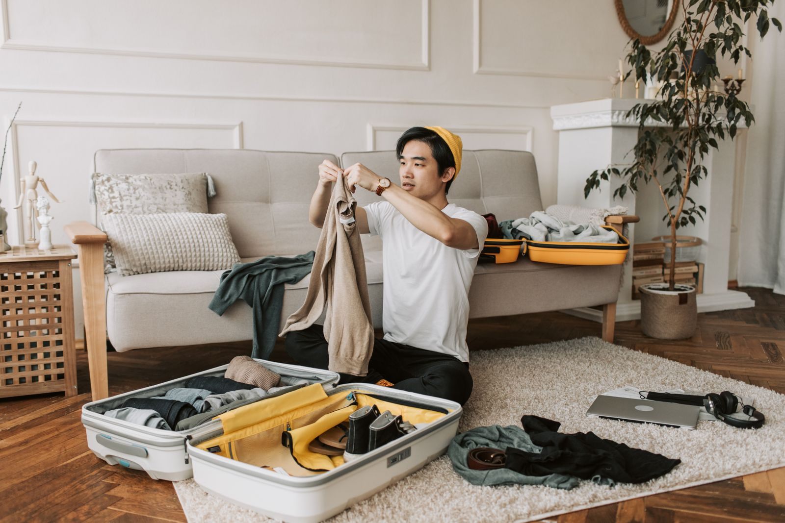 Man packing clothes into an open carry-on suitcase on a living room rug