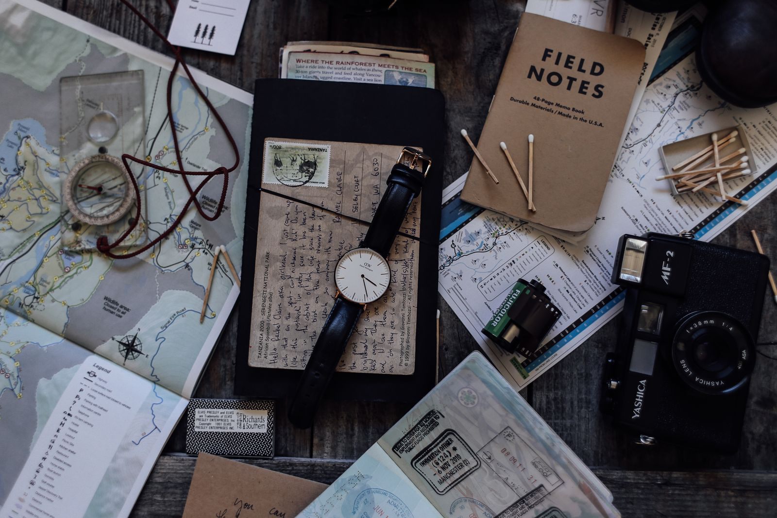 Travel planning flat lay with maps, a compass, a watch, a field notebook and a camera