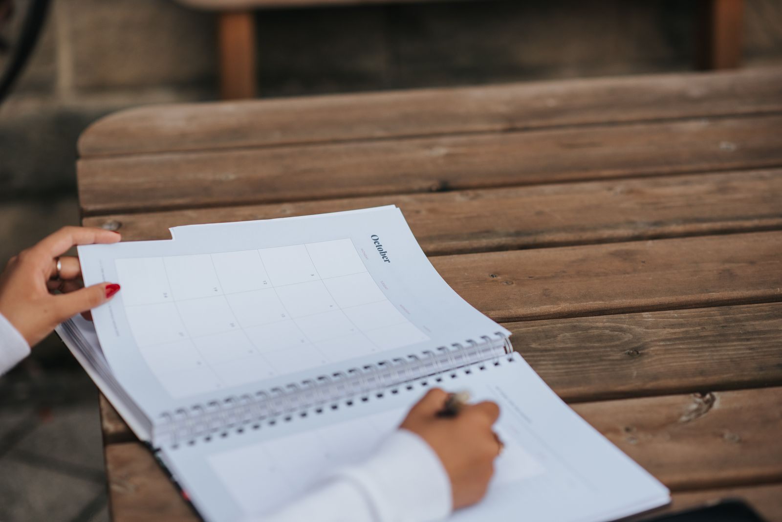 Person writing notes in a spiral notebook on a wooden bench